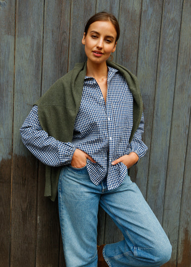 Woman wearing a green shawl over a checkered shirt and blue jeans against a wooden background