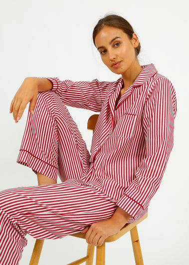 Woman wearing red and white striped pajamas sitting on a chair against a white background