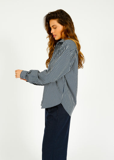 A woman wearing a navy and white striped, classic fit, button-down shirt with a collar and a breast pocket.