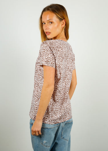 A woman wearing a leopard print cotton V-neck t-shirt in beige and light brown colors, paired with blue jeans.