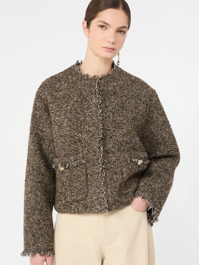 A woman modeling a cropped, long-sleeve tweed jacket in a brown and beige houndstooth pattern, paired with cream-colored trousers, against a plain white studio background.